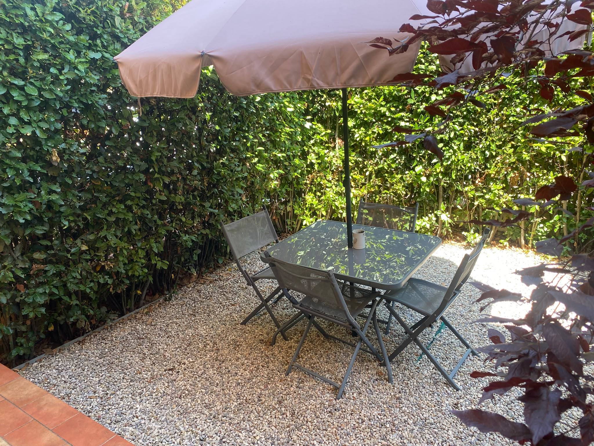 Patio in giardino con tavolo, sedie e ombrellone tra le siepi — B&B Lulù, Impruneta